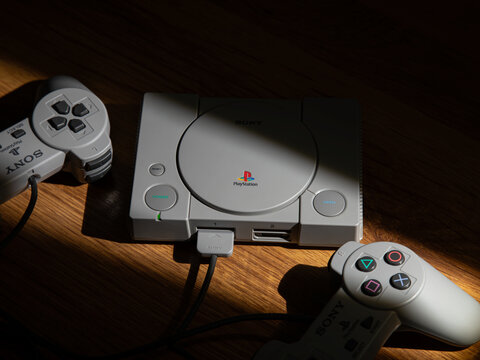 May 3, 2026, Odessa, Ukraine. Retro Sony PlayStation console with two controllers in dramatic sunlight on a wooden table.