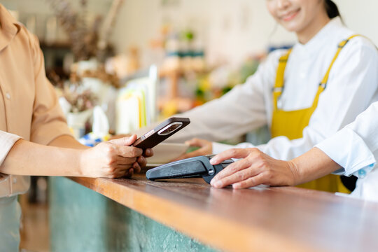 customer making contactless payment using mobile phone scan QR code at retail shop counter desk, asian clerk and buyer processing cashless digital technology smart phone paying NFC payment terminal