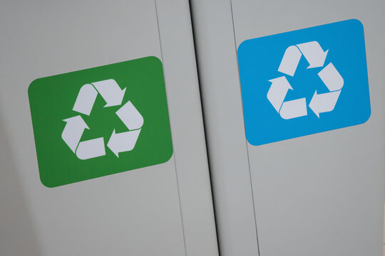 Blue plastic recycling symbol and green paper recycling symbols on a garbage can.