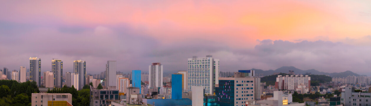 Gwangju City downtown skyline sunset panoramic aerial view in Jeollanam‑do, South Korea, with warm glowing clouds and sunrays over the Mudeungsan Mountain National Park