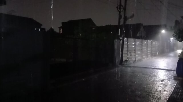 Nighttime street scene during rainfall with low visibility and street lighting, capturing a quiet and atmospheric rainy environment