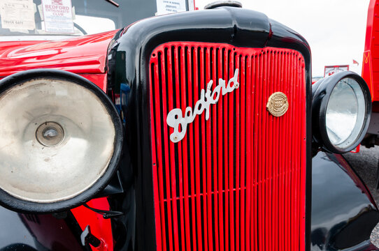 Vintage Bedford lorry front detail showing red vertical radiator grille, emblem badge, chrome headlight, and black mudguard
