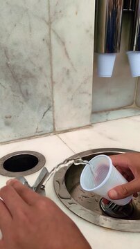 Filling a plastic cup with fresh zamzam water from a fountain tap. Vertical video.