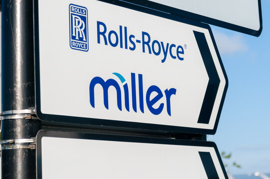 A directional road sign featuring the logos for Rolls-Royce and Miller, set against a clear blue sky