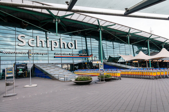 Main entrance facade of Amsterdam Airport Schiphol, showcasing modern glass and steel architecture with signage, signaling a busy international travel hub in the Netherlands.