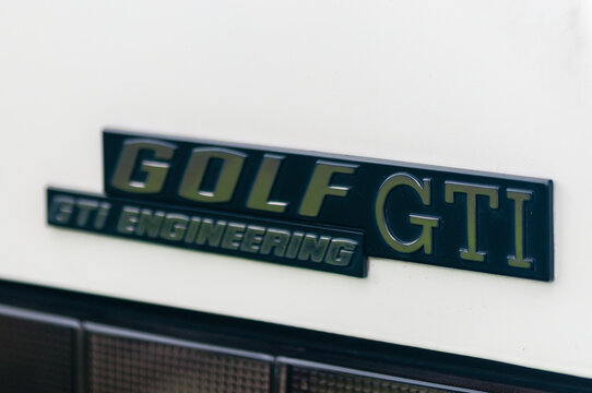 Close up of the iconic red and silver GTI badge on the black honeycomb radiator grille of a classic Volkswagen Golf Mk1, highlighting the heritage of the original hot hatch performance car.