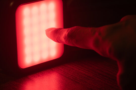 Macro shot of a hand reaching towards a glowing red LED light source in a dark environment, evoking concepts of energy, warning, or discovery