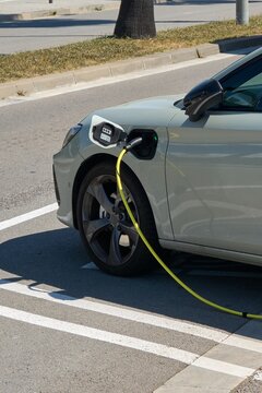A sleek gray hybrid vehicle is connected to a power supply at a public charging station in Catalonia, showcasing clean technology and eco-friendly transportation.