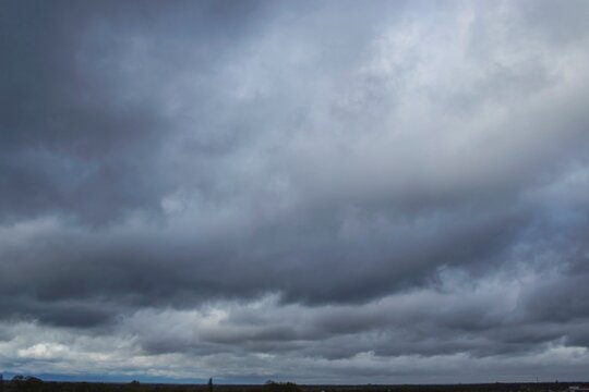 Stormy dark thunderclouds gather in the gloomy sky over the city. Cloudy sky with dark gray rain clouds.