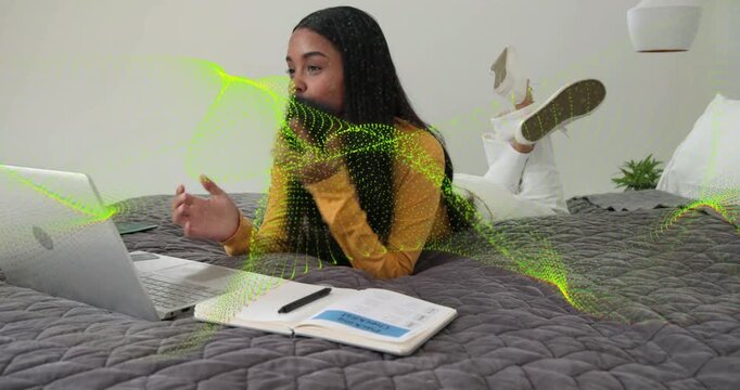 Woman lying prone reaching phone, starting call and noting for study, green particles overlaying