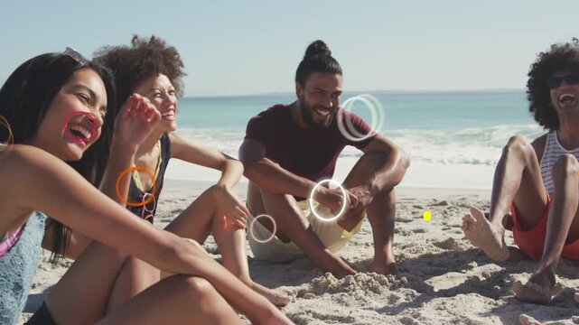 Four friends sitting on sand, chatting while bright shapes appearing near faces or hands for marketi
