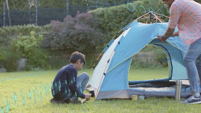 Father guiding son, son hammering stake while father locking poles, erecting blue camping tent
