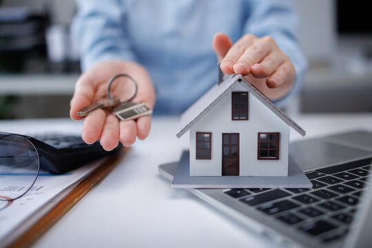 Hand protecting house model, holding keys on desk
