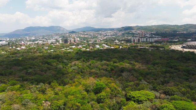 Big cloud shadow over  Parque de los Pericos in San Salvador, El Salvador, showing trees, urban parkland, buildings, and Estadio Cuscatlan. Cinematic cityscape and green space.