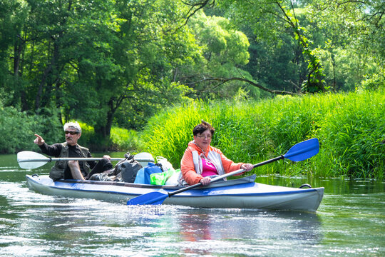 Senior couple on a Varzuga kayak, nature paddling adventure, mature travel, green riverbank, wellness and harmony.