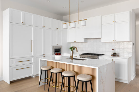 A kitchen detail with white cabinets and square tile backsplash, a waterfall marble countertop and wood slat panel front, and a gold light fixture, hardware, and faucet. No brands or labels.