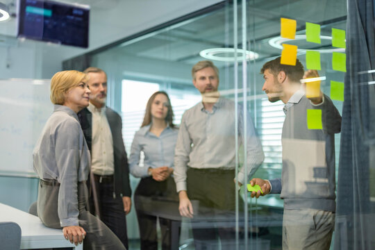 Businesspeople talking in their diverse team during a brainstorming session with sticky notes on glass wall in a modern office
