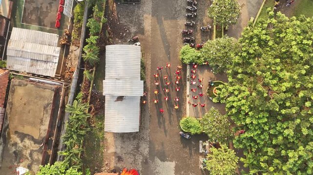 Vertical aerial zoom out of a synchronized exercise group in red shirts within a residential courtyard setting.