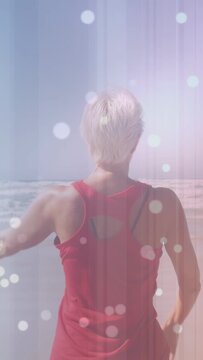 Vertical video: Woman breathing, swinging right arm and stretching for fitness, red top, sea, bokeh