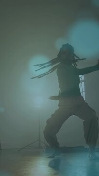 Vertical video: Dancer starting routine practicing dance turns and kicks in lit studio, teal bokeh