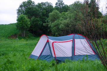 Single red and grey tent in wild grassy field, surrounded by trees, tourism, solo camping, nature recreation and exploration setting. © Ольга Симонова