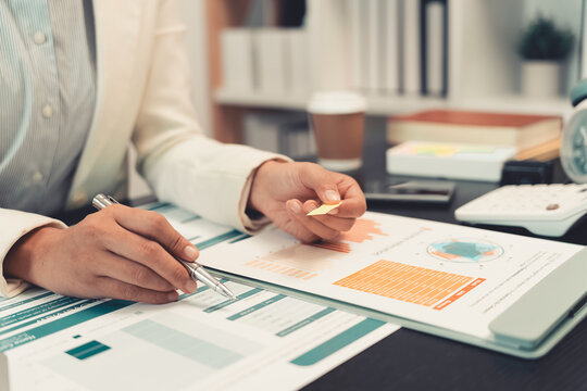 A Muslim businesswoman is working with financial graphs and a computer, remotely from a modern office.