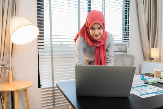 A Muslim businesswoman is working with financial graphs and a computer, remotely from a modern office.