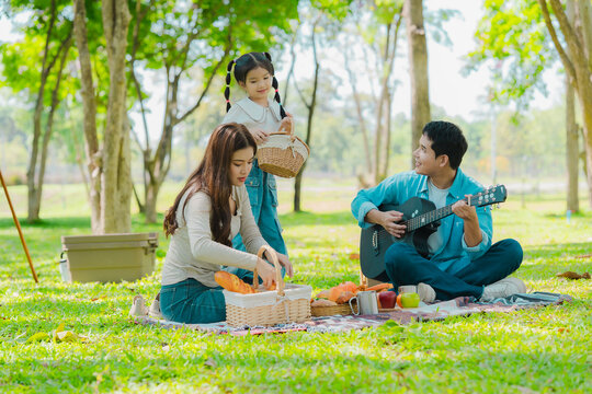A family of three from Asia enjoyed using their laptops in the park and also enjoyed a picnic together in the park.