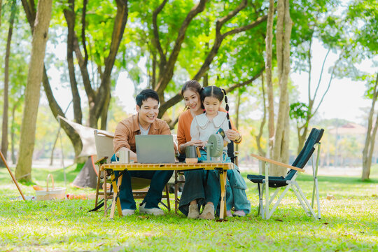 A family of three from Asia enjoyed using their laptops in the park and also enjoyed a picnic together in the park.