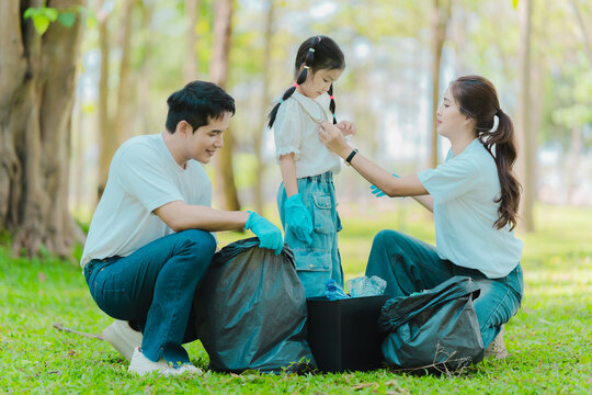 Environmental conservation concept: A cute little girl and her parents are picking up trash in the park. A family of volunteers is collecting trash in the forest. Environmental conservation concept.
