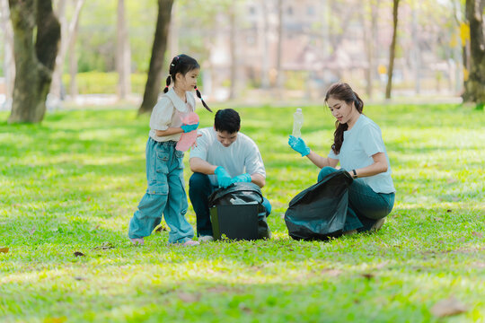 Environmental conservation concept: A cute little girl and her parents are picking up trash in the park. A family of volunteers is collecting trash in the forest. Environmental conservation concept.
