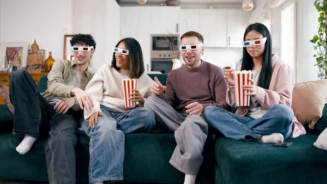 Cheerful young friends wearing 3d glasses while sitting on a couch and enjoying a movie. Four people eating popcorn and laughing together