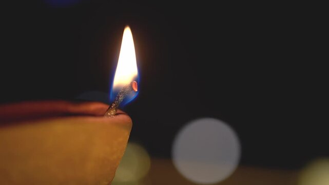 Macro shot of flame from cotton oil soaked wick in a earthenware clay diya set against a background with light bokeh showing the simple traditional decorations during diwali in India