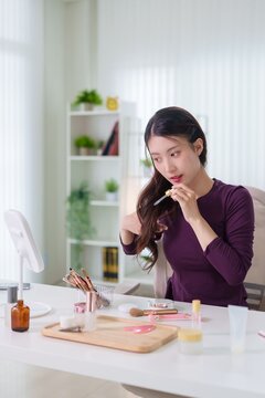 Asian women beauty influencer applying makeup cosmetics product at home office desk recording tutorial video content creator lifestyle modern bright interior