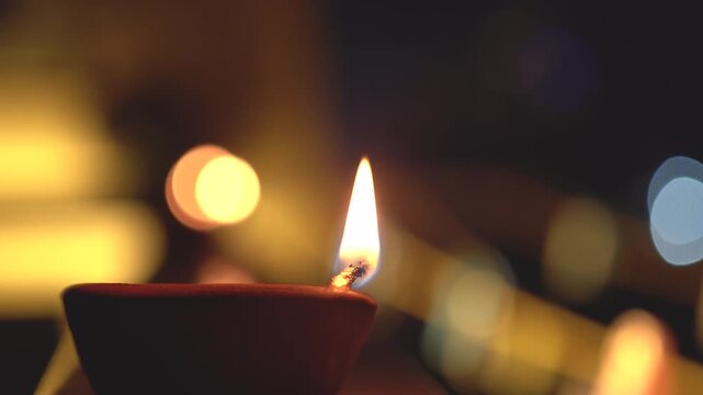 Macro shot of flame from cotton oil soaked wick in a earthenware clay diya set against a background with light bokeh showing the simple traditional decorations during diwali in India