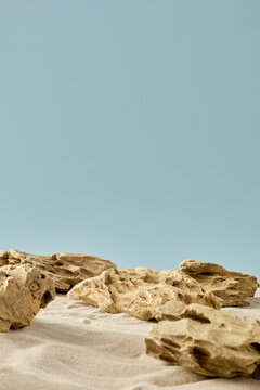 Empty podium for products: natural stones on sand against a blue background. Minimalist landscape for beauty, jewelry, or organic brand mockups