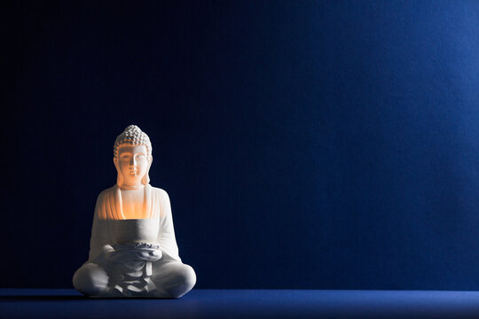 Minimalist Zen scene featuring a white Buddha statue with a glowing light against a deep blue background with ample copy space for text