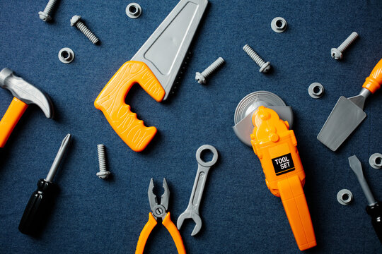 Top view of various colorful toy tools like an angle grinder, saw, and wrench scattered across a blue background. High-angle shot showcasing a complete handyman play set.
