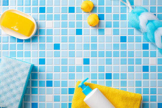 Kids bath time fun frame: rubber ducks, blue sponge, yellow soap, and baby lotion around empty mosaic tiles. Ideal for children's hygiene branding or announcements