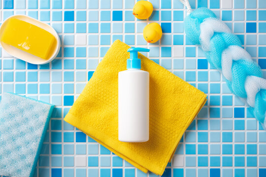 Essential baby bath kit: white pump dispenser, yellow towel, rubber ducks, soap, and sponge on colorful mosaic tiles. Perfect for new parents or kids product lines