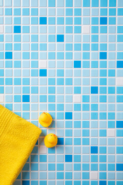 Baby bath minimalism: two classic rubber ducks and a corner of a soft yellow towel on blue mosaic tiles. Simple, fun composition for infant product branding.