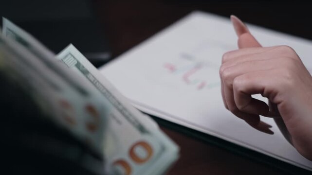 Close-up of cash bundles placed beside a notebook as a hand writes notes, showcasing a financial transaction in a modern office setting