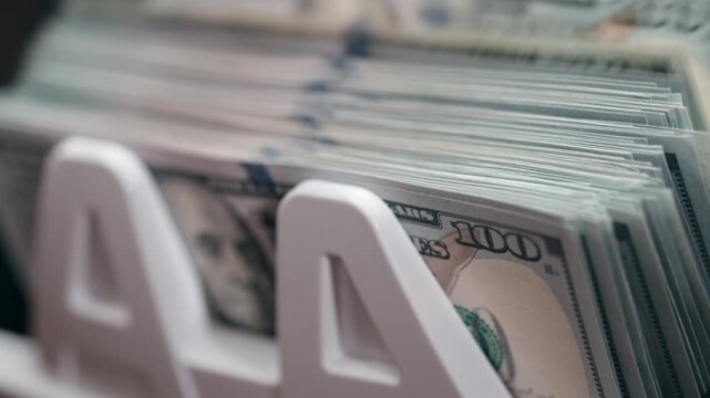 Close-up of 100 dollar banknotes being counted by an automatic money counting machine, crisp bills moving rapidly through device. Concept financial operations and cash processing technology.
