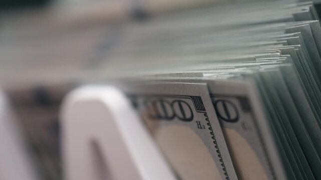 Close-up sequence of US dollar bills stacked in a white money holder, showcasing the detailed texture and design of the currency in a well-lit indoor setting