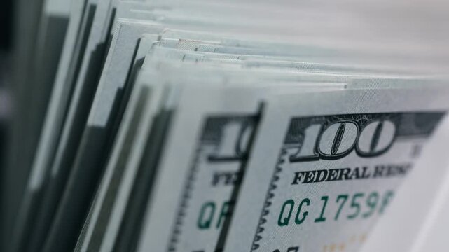 Close-up sequence of US hundred dollar bills being fanned out, showcasing the intricate details of the currency and the texture of the paper in a well-lit setting