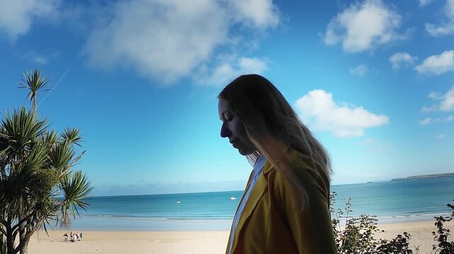 A woman walks on the evening seaside wearing yellow jacket