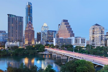 Fototapeta premium Austin Downtown Skyline at Dusk with Illuminated Skyscrapers, Congress Avenue Bridge Traffic Trails, and Reflections Over Lady Bird Lake in Texas
