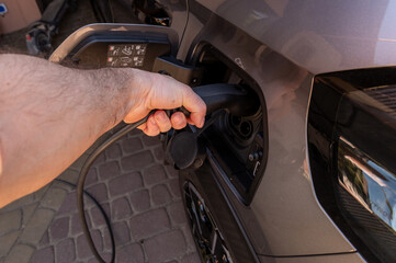 Electric car charging cable being plugged in close-up Close-up of a person connecting a charging cable to an electric vehicle. Concept of sustainable transport, clean energy and modern mobility. © Micha