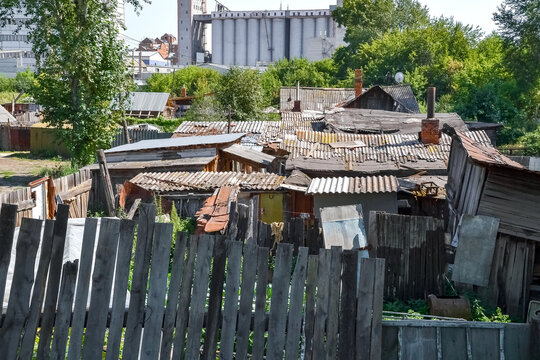 Old wooden shacks and fences in a poor neighborhood with industrial buildings in the background