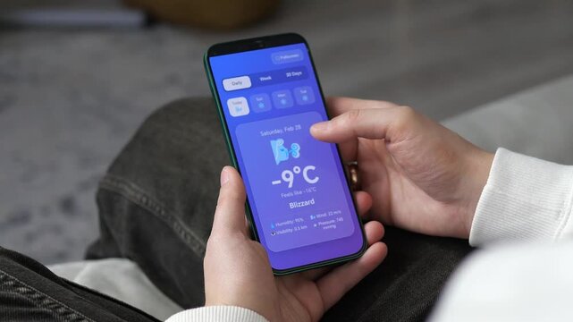 Winter weather alerts on smartphone. User scrolls through extreme conditions from cloudy to blizzard and heavy snow. Ideal for weather reports, travel safety, and mobile app marketing. Sleek purple
